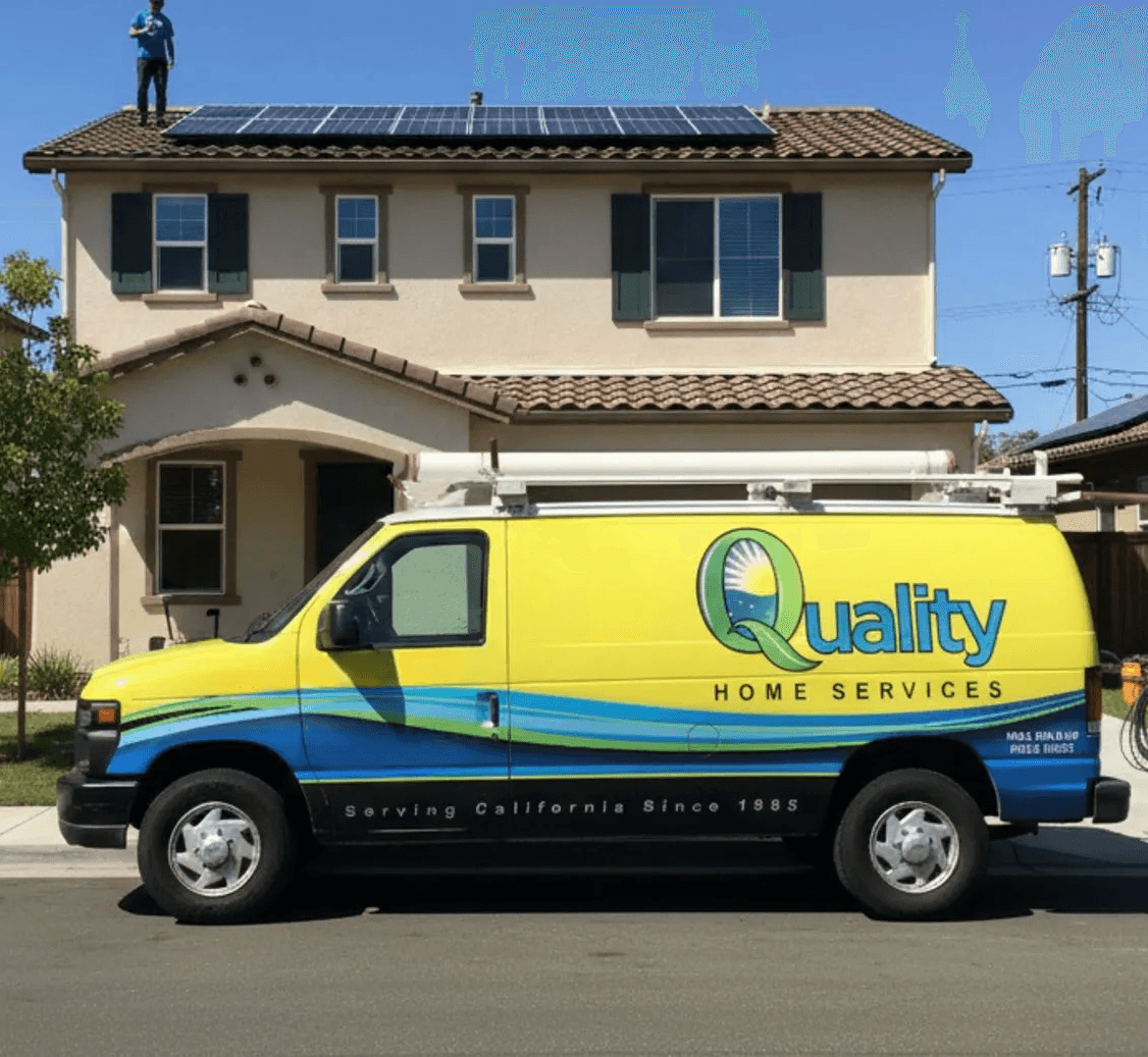 A yellow Quality Home Services van is parked in front of a house with solar panels. Workers in blue shirts are installing equipment, conveying professionalism.
